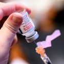 仔细的观察一个人的手指拿着瓶疫苗卷入一根针