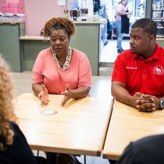 一个女人在一个粉红色的衬衫坐在一个男人旁边一个红色衬衫从威斯康辛大学麦迪逊分校总理Mnookin桌对面,穿着黑色衬衫开云体育appios下载