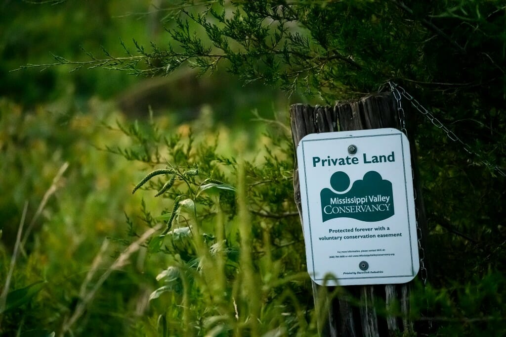 白色和绿色标志标识私人土地,是密西西比河流域保护的一部分。黄色的花在背景。
