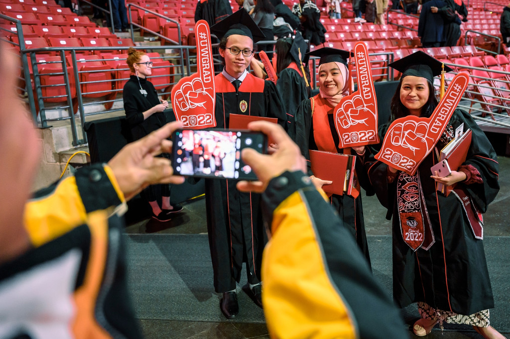 穿着毕业礼服的人们对着前景中用手机拍照的人微笑。